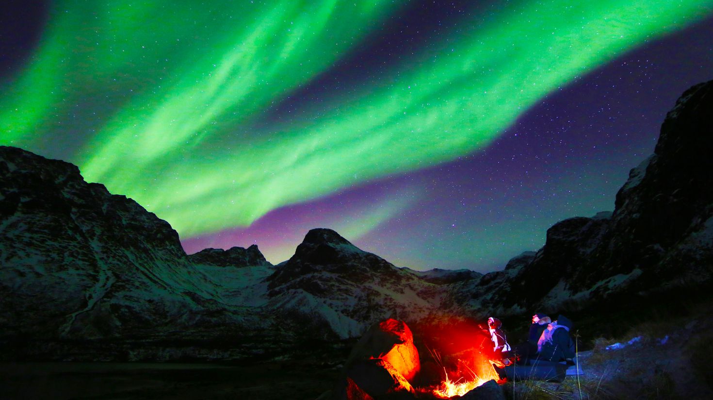 Tourists amidst mountains watching green lights in the night sky