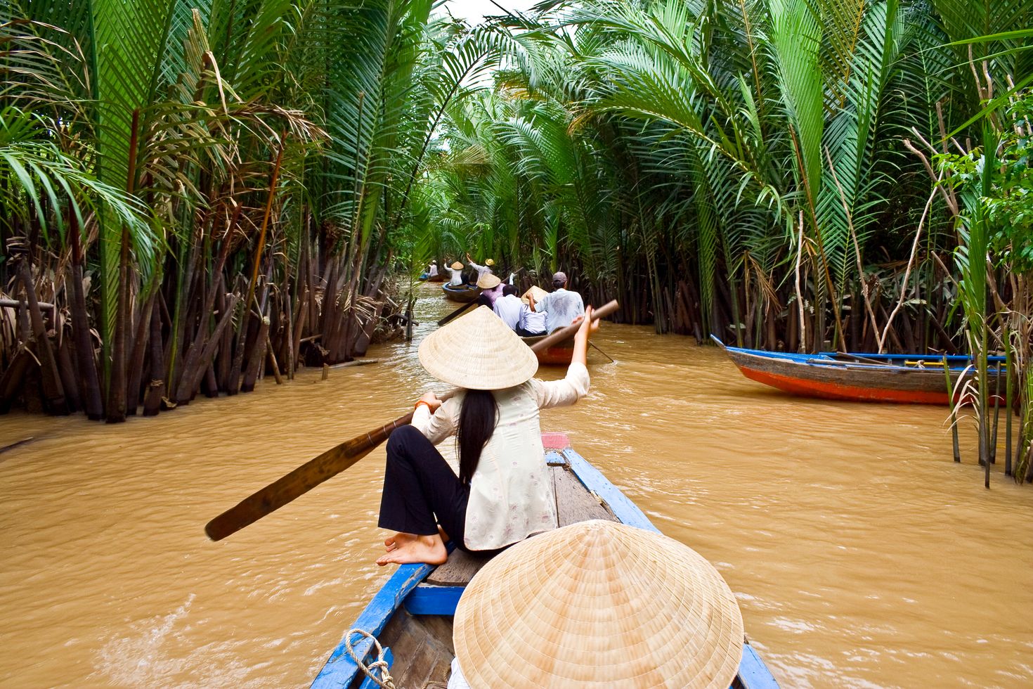 A Vietnamese woman rowing a boat behind other boats with tourists.
