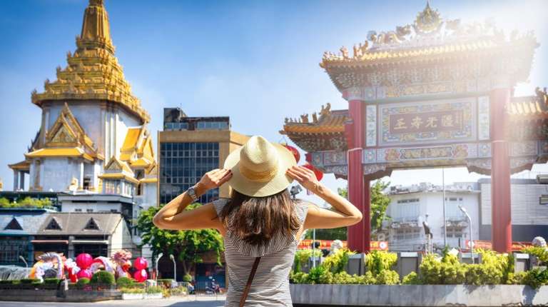 A travel influencer in Asia stands in front of Chinatown Gate in Bangkok.