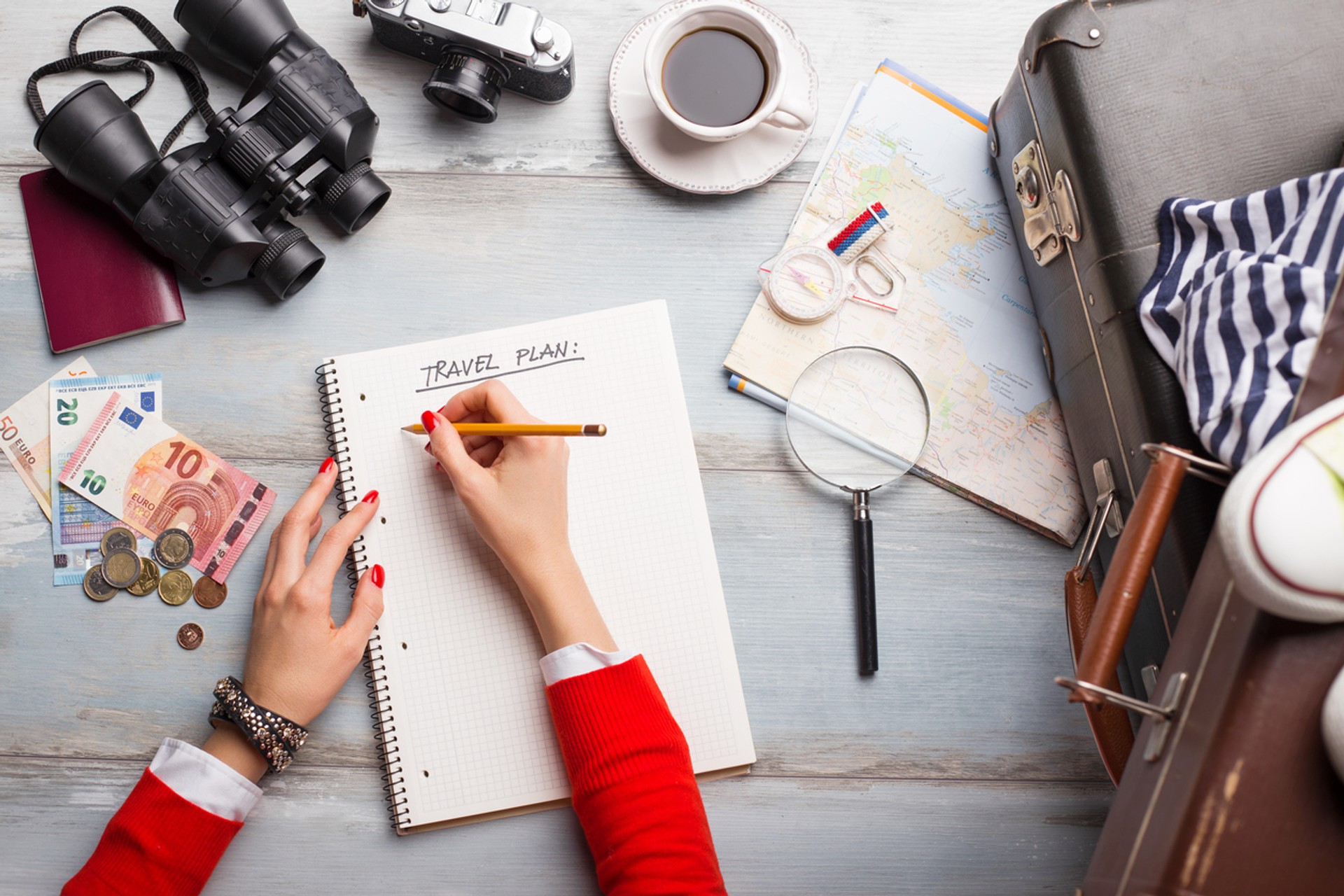 A woman listing out things to do on her notebook on her desk planning her trip.
