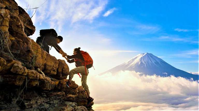 A hiker helps his friend climb up the hill during their travel.
