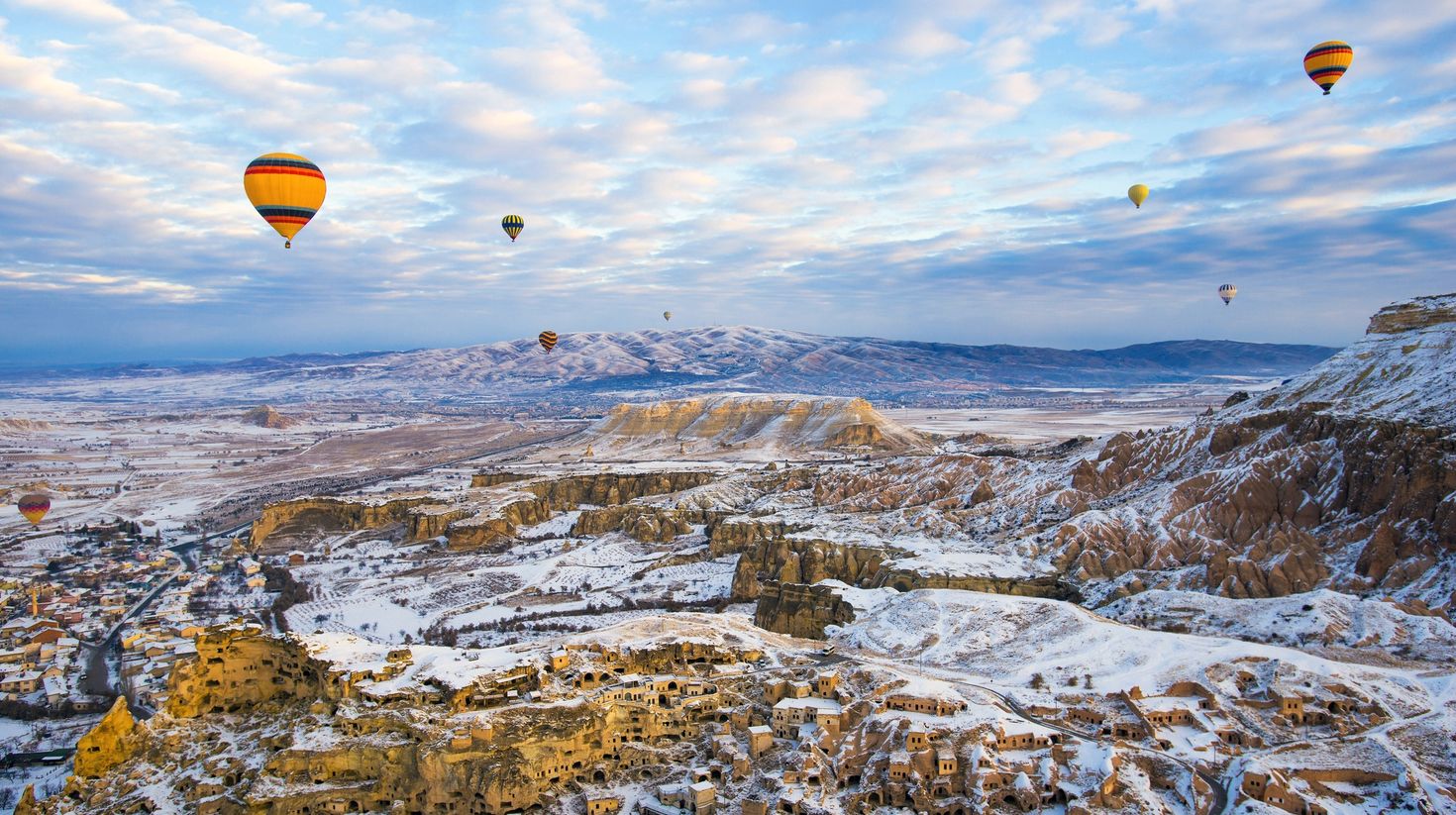 Hot air balloons flying in Cappadocia with snow on the landscape.