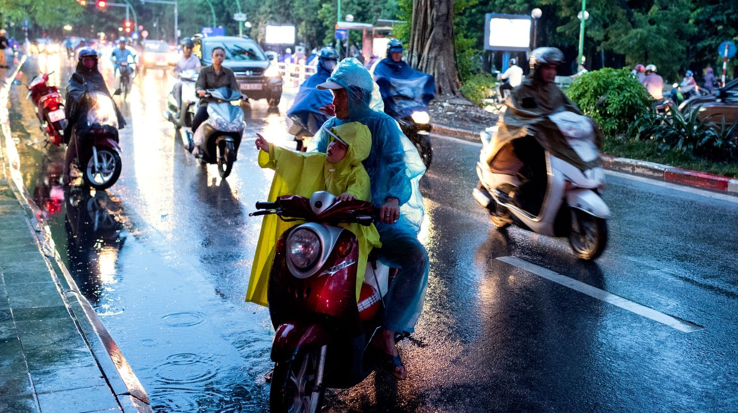 Boy pointing while riding a scooter with his father in Vietnam in September