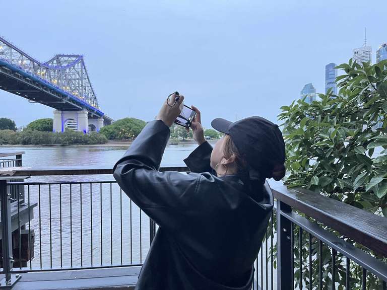 A woman in a black cap takes a picture of the bridge in Sydney