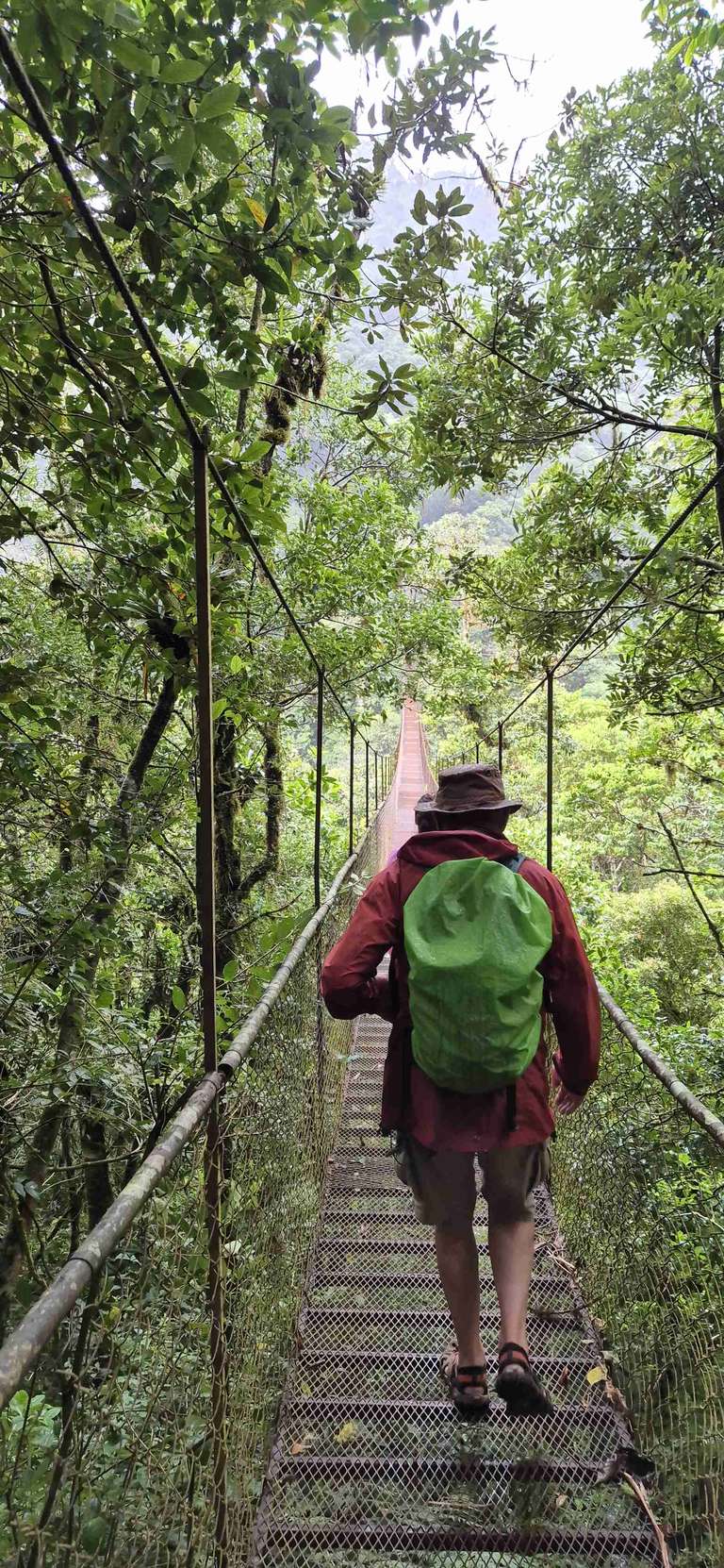 A man with green backpack walks down handing bridge over Monteverde forest