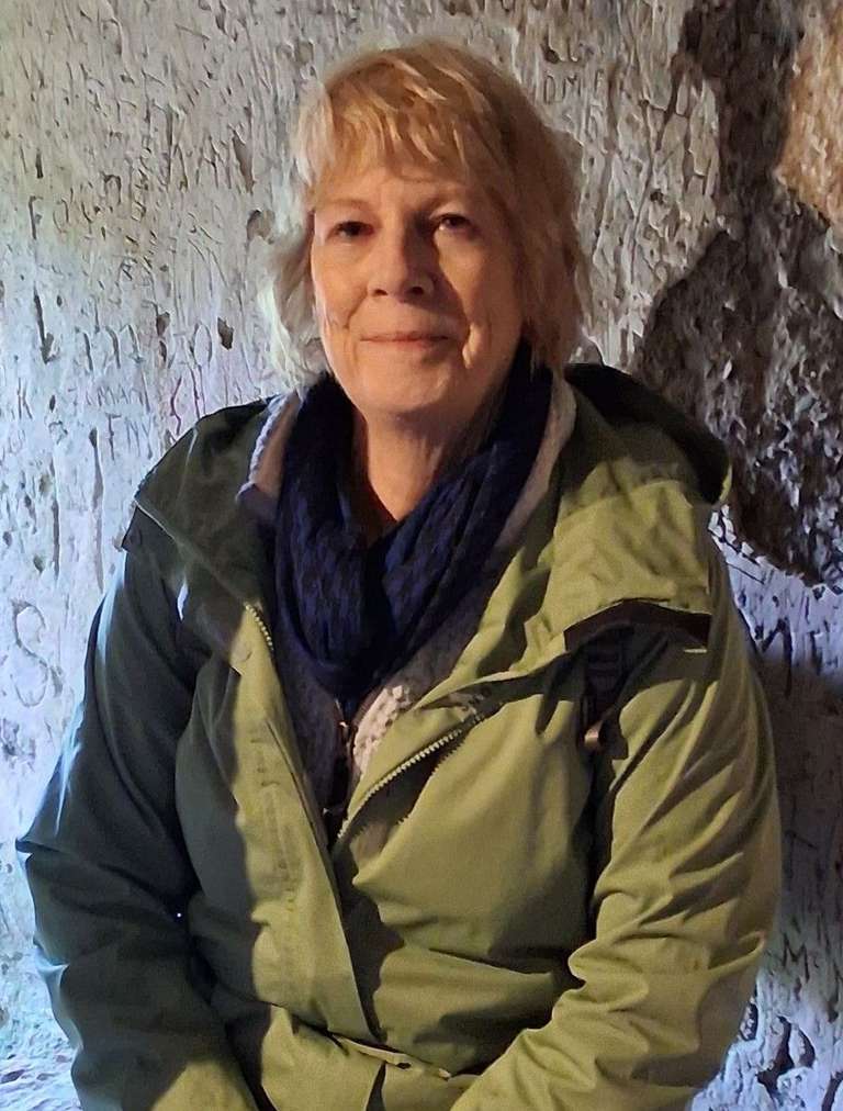 An older lady in green jacket poses inside an old building
