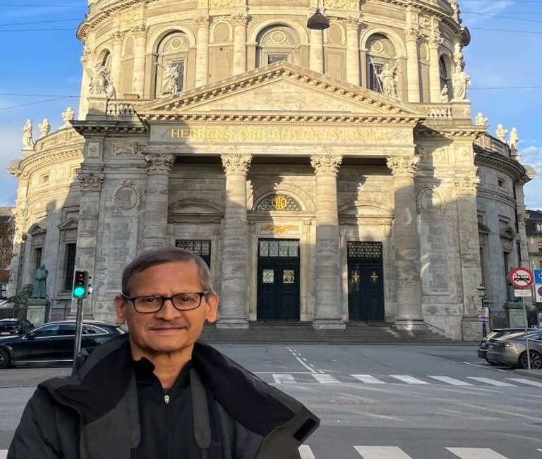 An elderly man poses in front of an ancient European structure