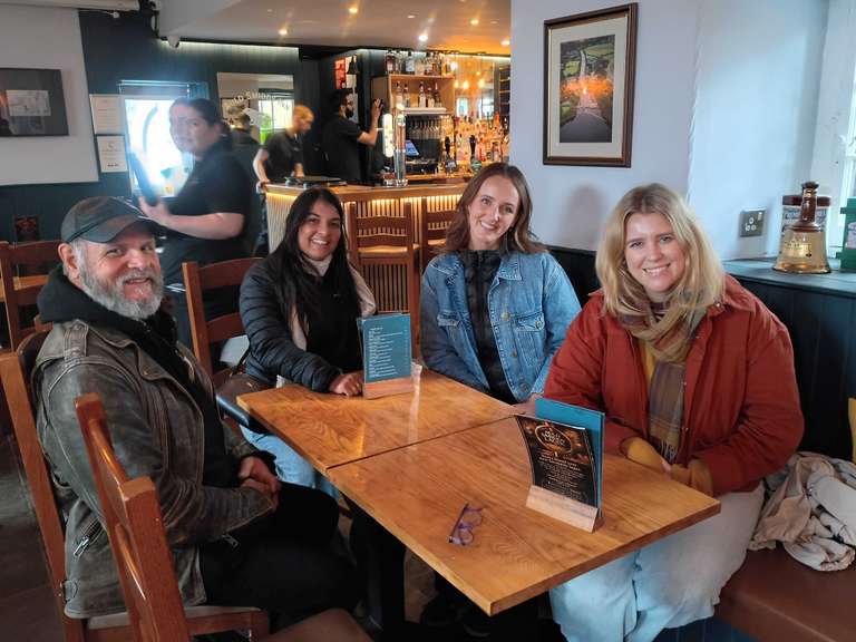 Four travelers of different ages sit around a table in a restaurant with the waiter seen in the background