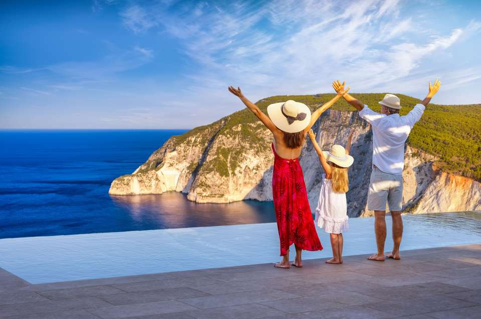A happy family on summer holidays enjoys the sunset view over the ocean from their swimming pool