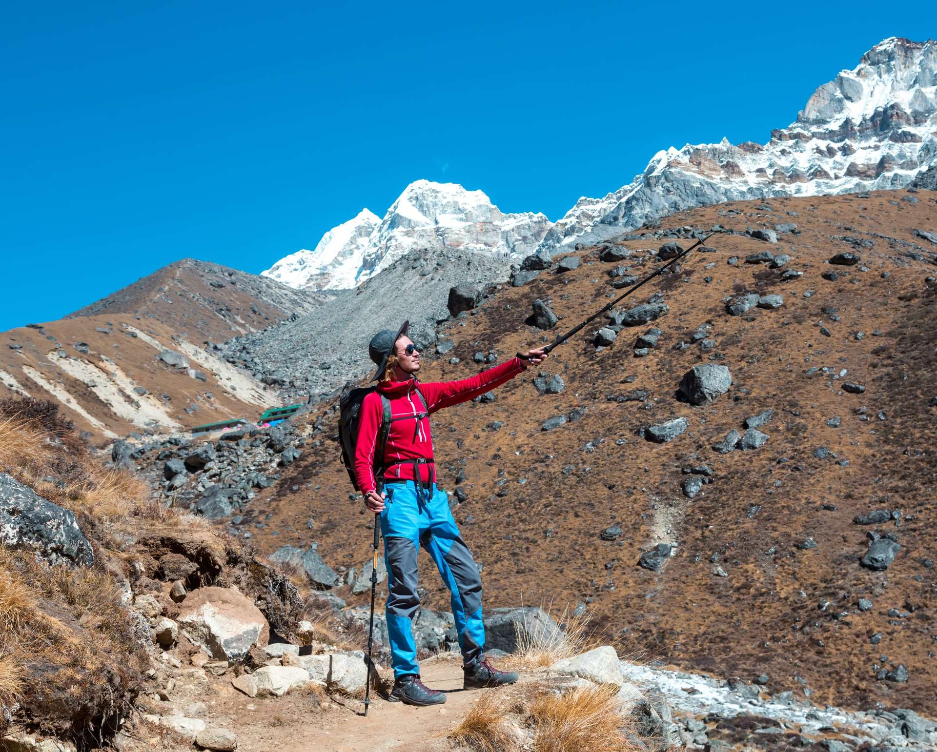 Young male Hiker pointing on Mountain Summit with walking Stick