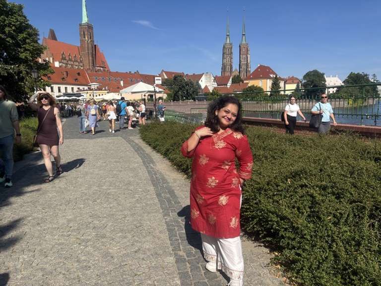 A woman in red and white outfit poses against the backdrop of a city in Poland