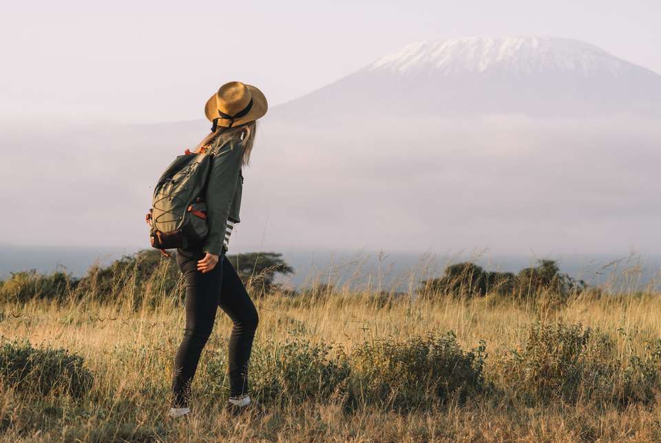 Stylish hipster girl in hat walking against the backdrop of peak of Kilimanjaro